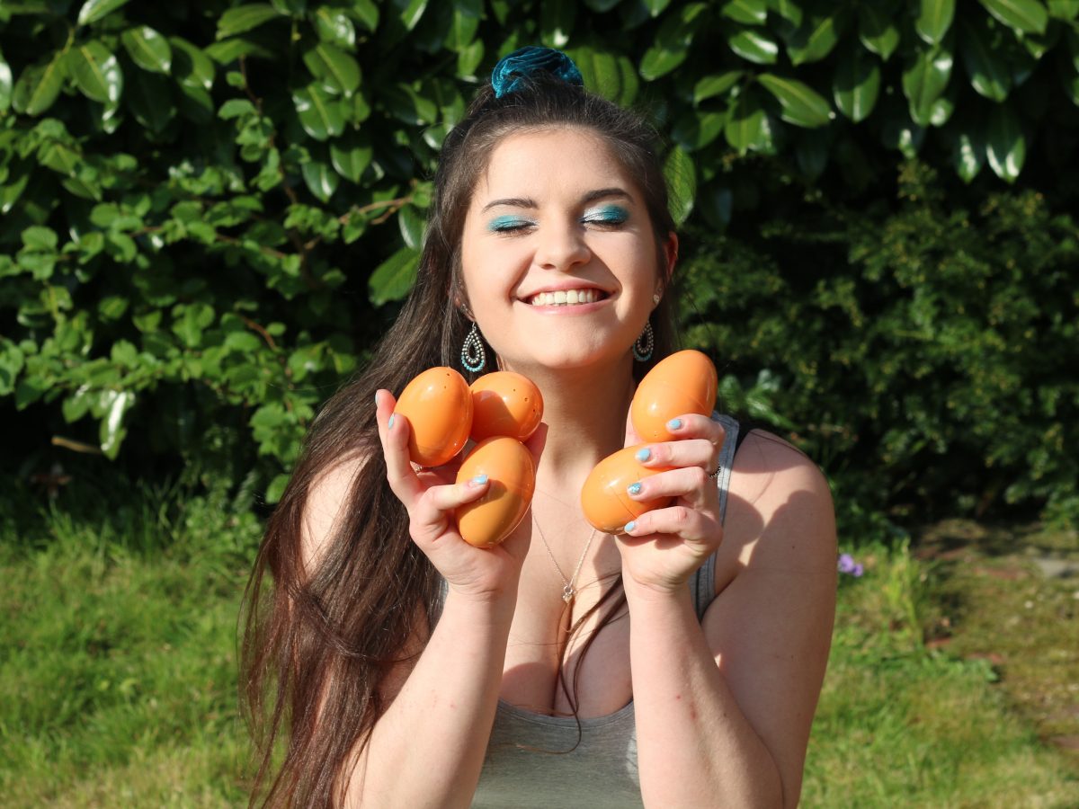 Maude smiles at the camera with her hands full of orange plastic eggs